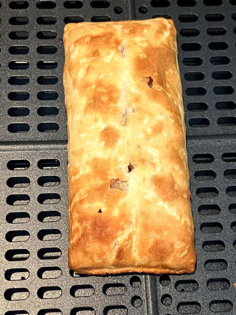 Close-up of a single golden-brown pizza stick in the air fryer basket, showcasing its crisp, flaky crust.