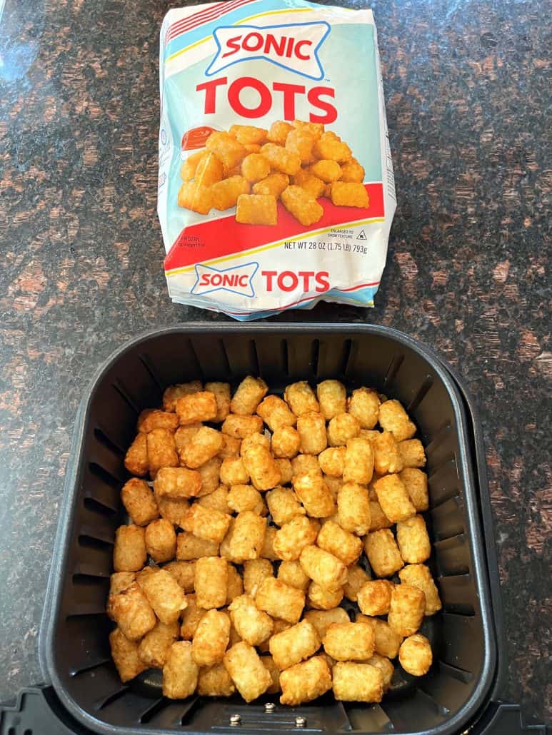 Air fryer basket filled with crispy, golden Sonic tater tots next to the packaging.