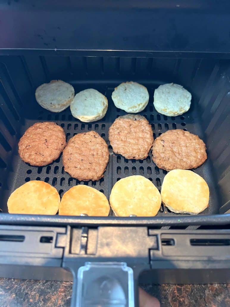 Air fryer basket with evenly spaced sausage patties and biscuit halves, showing the step of separating components for even cooking in the recipe.