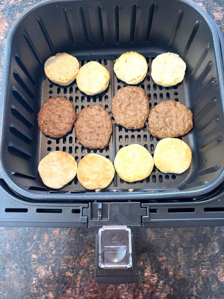 Air fryer basket filled with biscuit halves and sausage patties arranged.