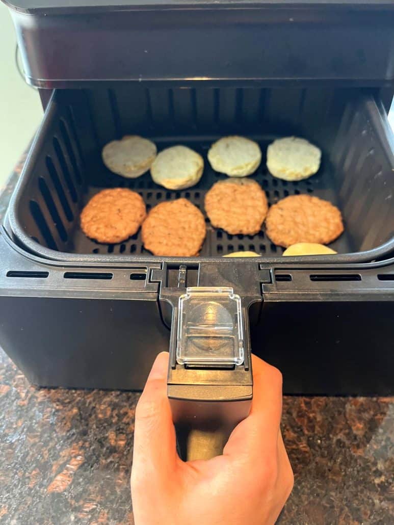 Air fryer basket with separated sausage patties and biscuit halves, illustrating the preparation step for cooking Jimmy Dean Biscuit Sausage Sandwiches in the air fryer.