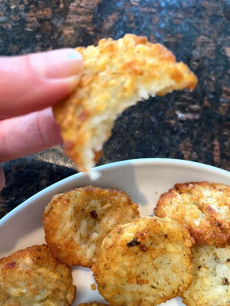 Hand of Melanie Mendelson from melaniecooks.com holding a bitten McCain Baby Cakes Hashbrown, revealing the crispy exterior and fluffy interior.