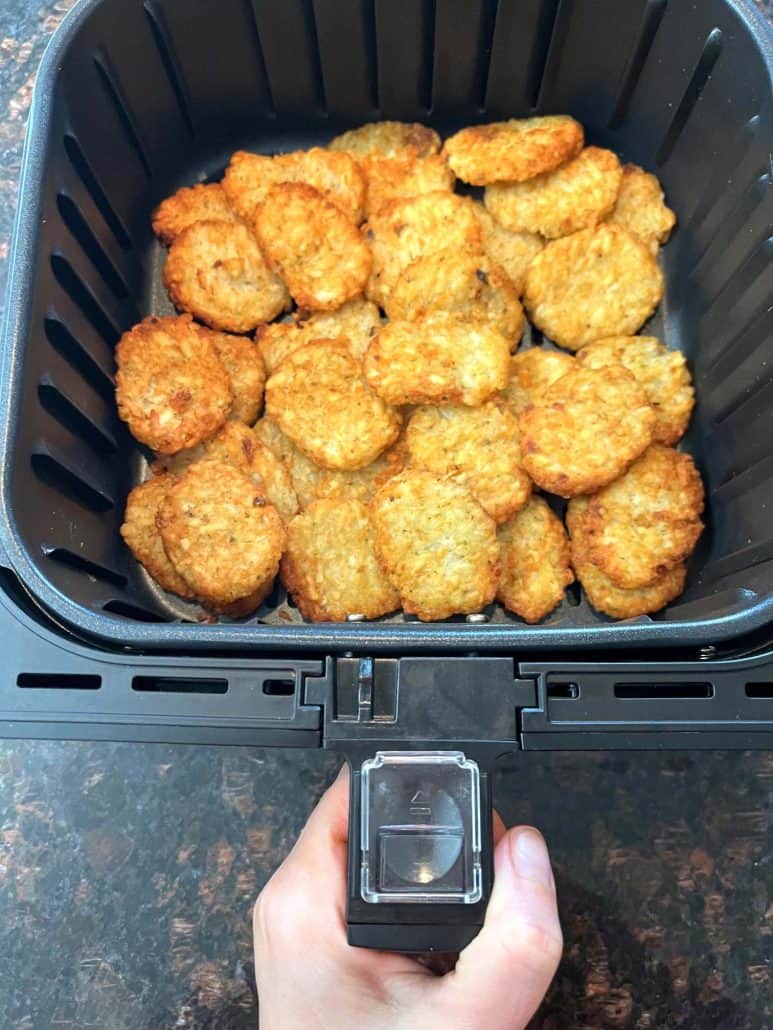 Hand of Melanie Mendelson from melaniecooks.com holding an air fryer basket filled with perfectly cooked, golden McCain Baby Cakes Hashbrowns. 