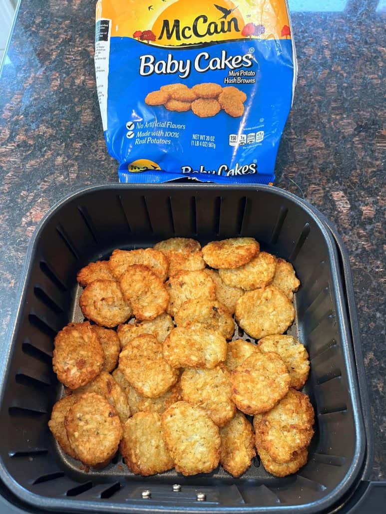 Cooked McCain Baby Cakes Hashbrowns in an air fryer basket with the package displayed in the background.