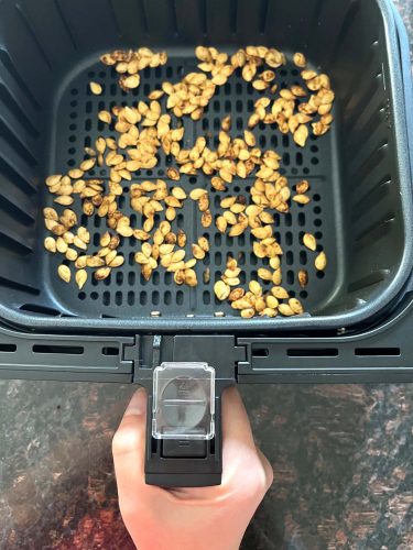 Freshly roasted pumpkin seeds in an air fryer basket, golden and crispy, ready to enjoy as a healthy snack.