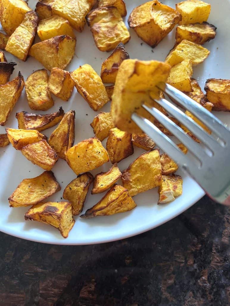 A fork lifting a perfectly roasted air-fried pumpkin cube from a plate.