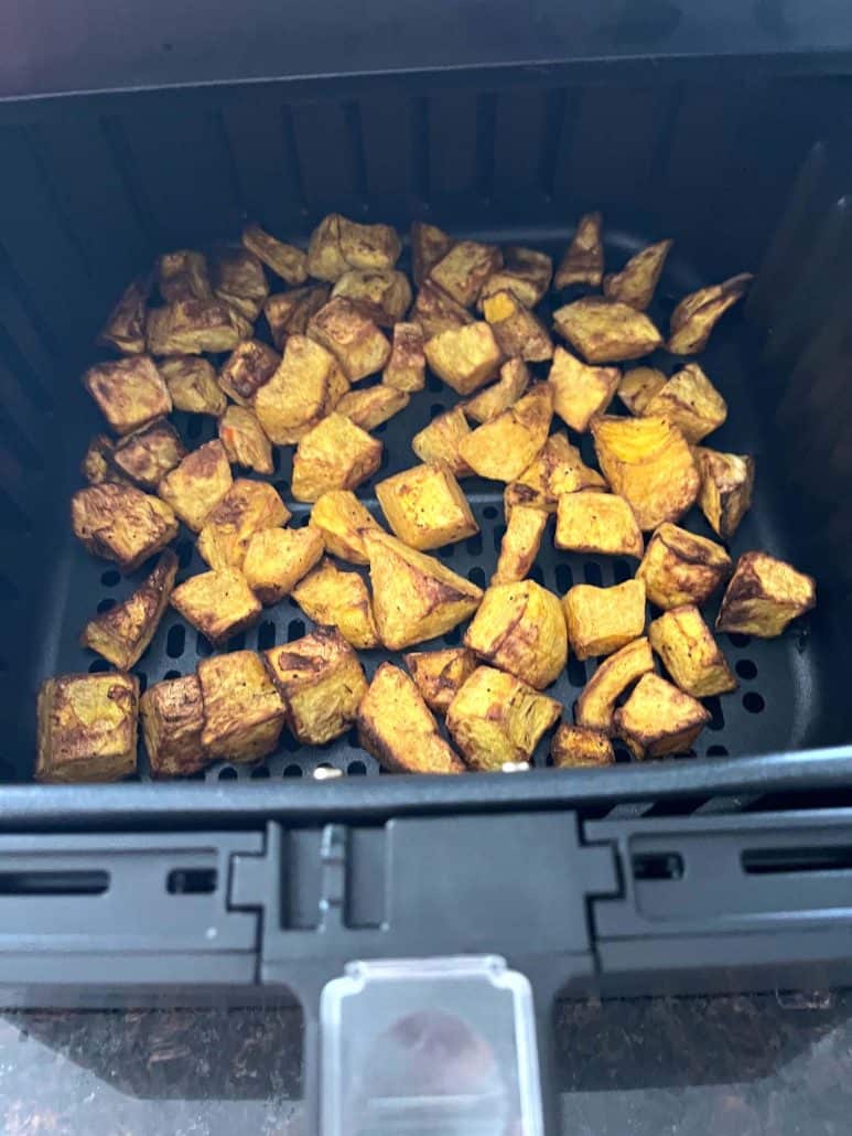 Golden-brown color and crispy texture of roasted pumpkin cubes in an air fryer basket.