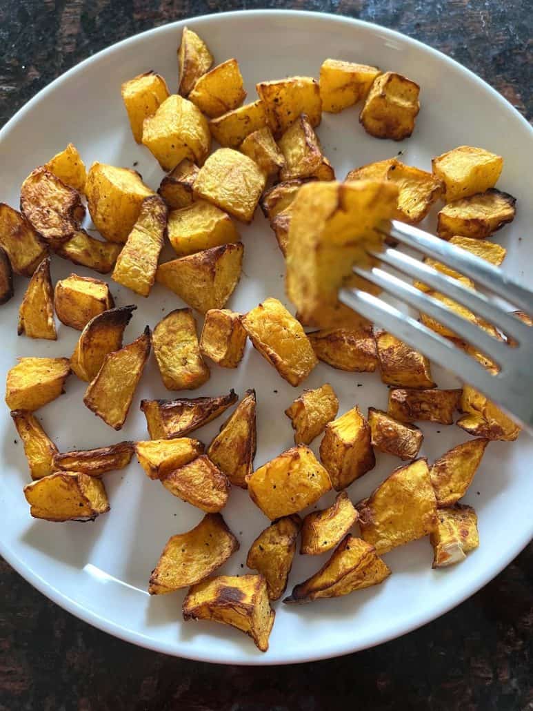 Fork holding a crispy, golden piece of air-fried pumpkin above a plate filled with roasted pumpkin cubes.