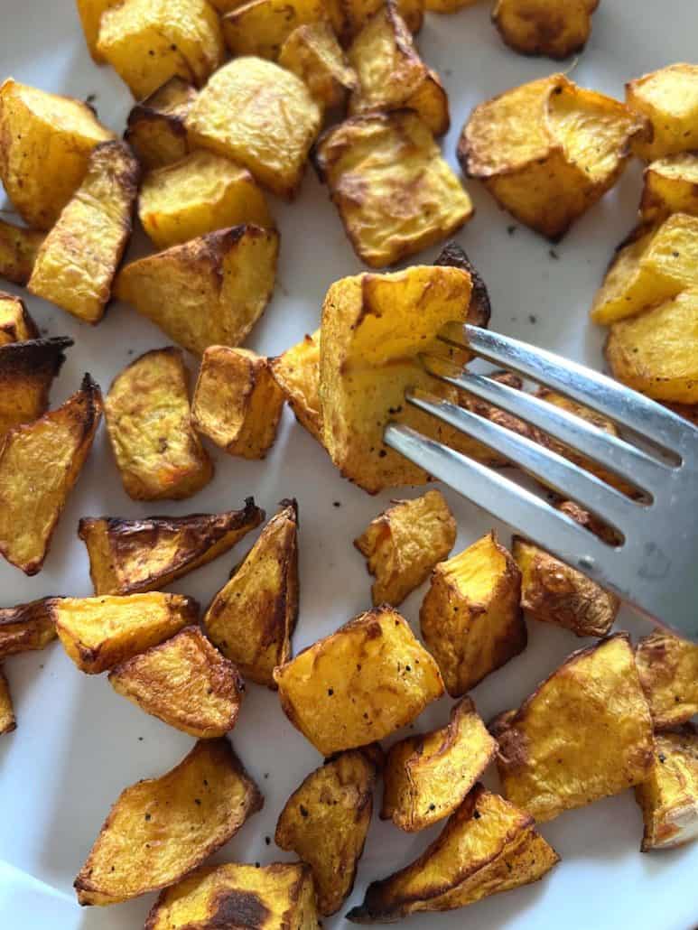 Close-up of fork picking up a golden piece of air-fried pumpkin from a plate of roasted cubes, highlighting the savory, seasoned texture of the dish.