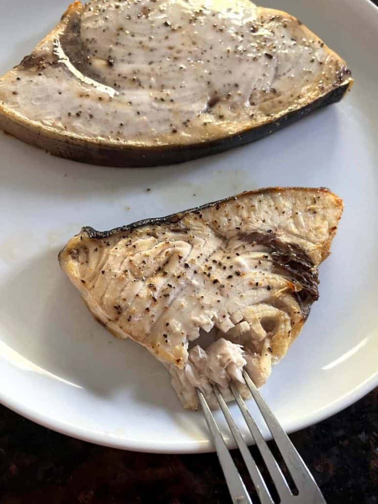 A fork breaking into a tender, flaky air-fried swordfish fillet on a white plate, highlighting the perfectly cooked texture.