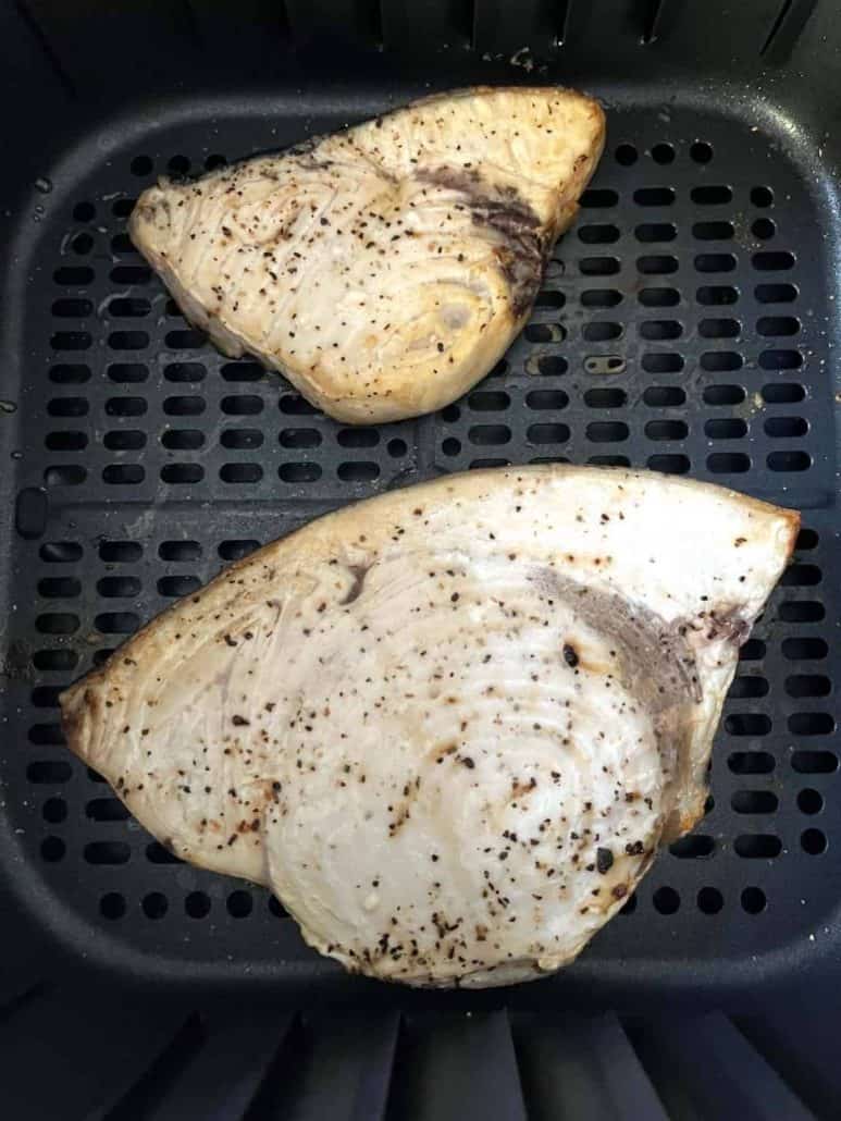 Seasoned swordfish fillets, flaky finish arranged in an air fryer basket.