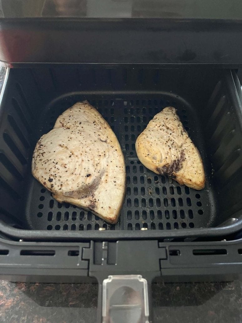 Two swordfish fillets in an air fryer basket, seasoned and ready for cooking.