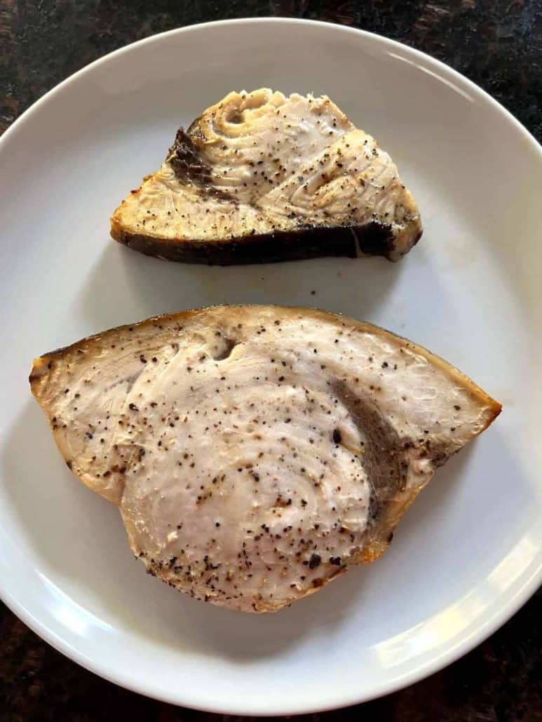 Two air-fried swordfish fillets served on a white plate, showcasing their perfectly cooked, seasoned surface.