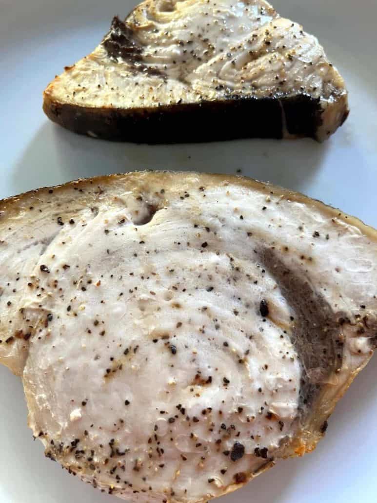 Close-up of two seasoned air-fried swordfish fillets on a white plate, highlighting the golden, cooked texture and simple seasoning.