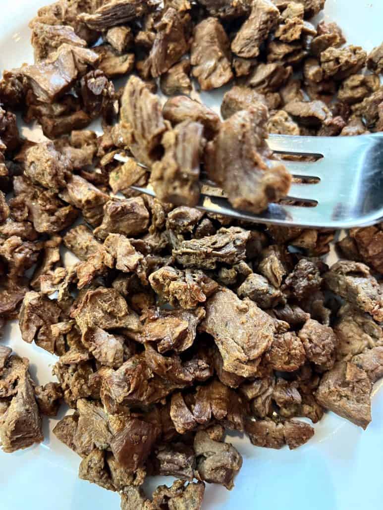 A fork lifting a piece of cooked Beyond Steak Tip from a plate full of the plant-based steak tips, highlighting their texture and appeal as a vegan alternative.