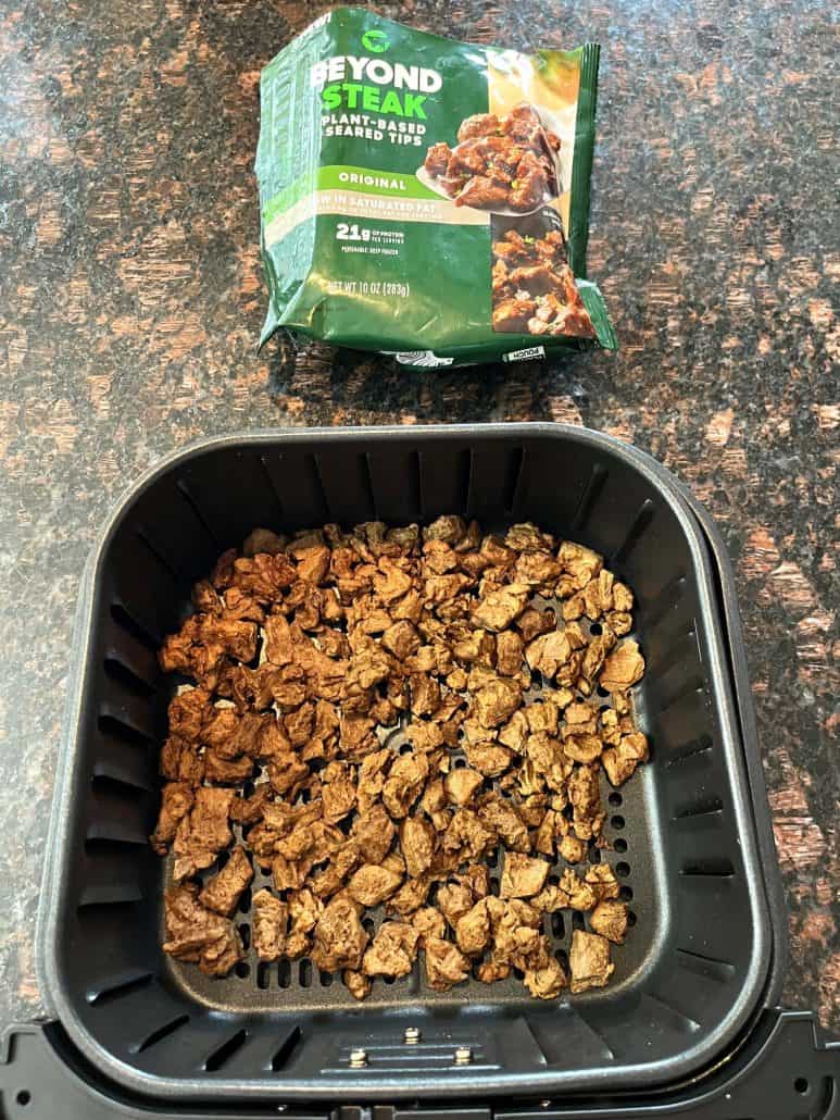 Cooked Beyond Steak Tips in an air fryer basket with the packaging placed in the background.