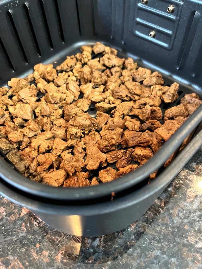 Close-up of cooked Beyond Steak Tips in an air fryer basket, highlighting their crispy and golden texture.