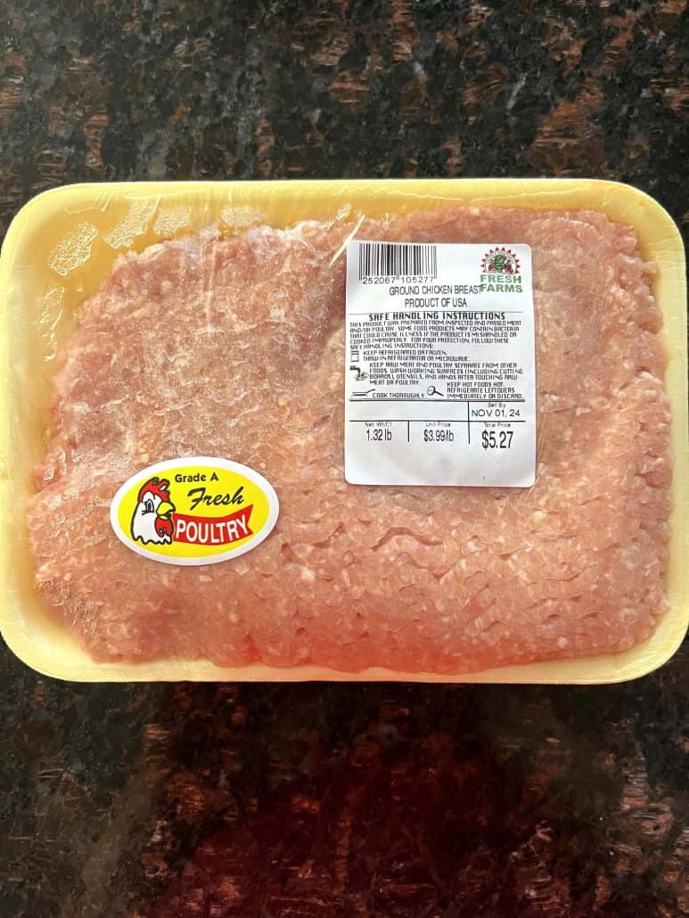 Package of raw ground chicken breast, ready to be cooked in a frying pan.