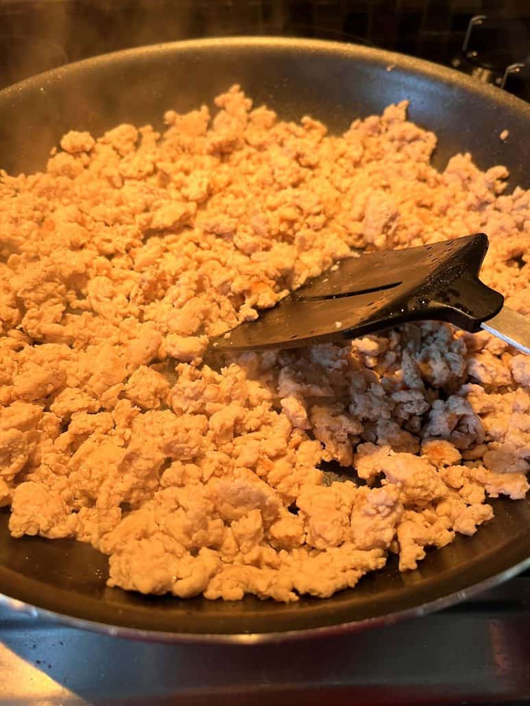 Ground chicken cooking evenly in a frying pan, with a spatula used to break up the pieces for a perfect, crumbly texture.