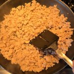 Ground chicken cooking in a frying pan, broken up with a spatula to ensure even cooking and a crumbly texture.