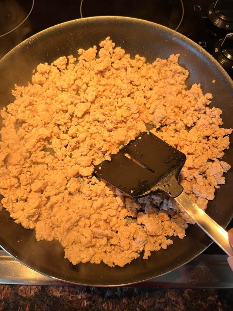 Ground chicken cooking in a frying pan, broken up with a spatula to ensure even cooking and a crumbly texture.