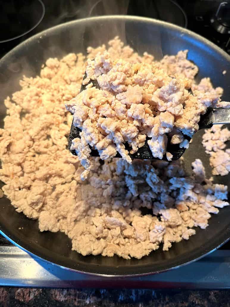 Ground chicken cooking in a frying pan, with a spatula lifting the pieces to show even browning and thorough cooking.