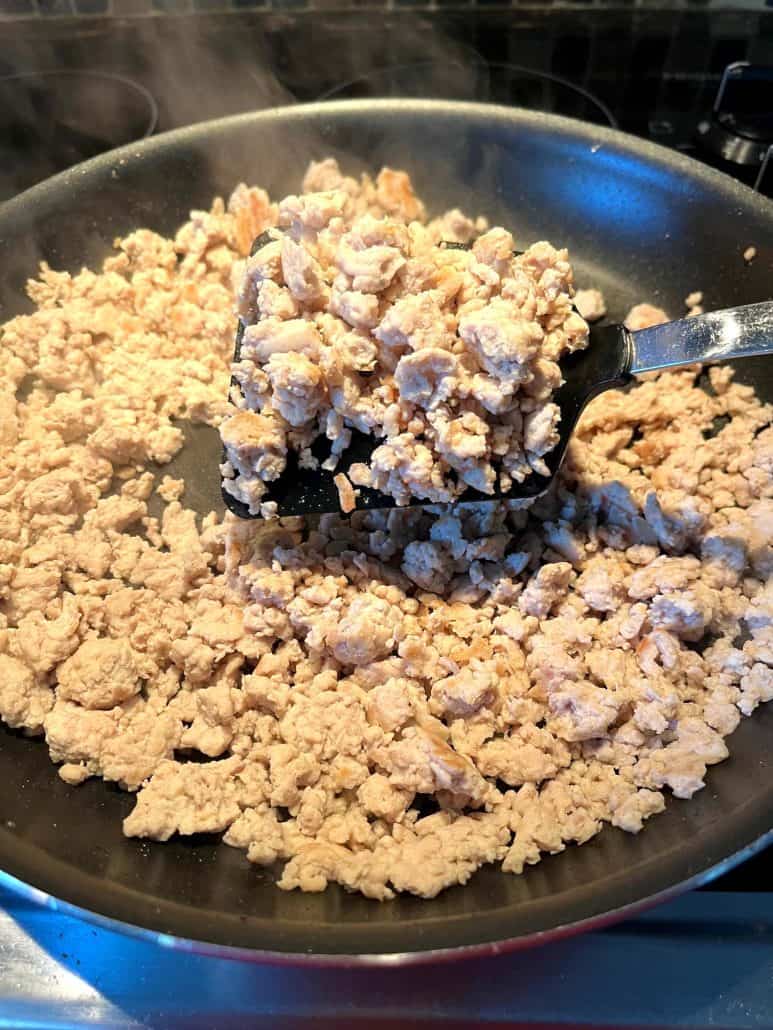 Cooked ground chicken in a frying pan, lifted by a spatula to show the uniform white color indicating it's fully cooked and ready for seasoning.