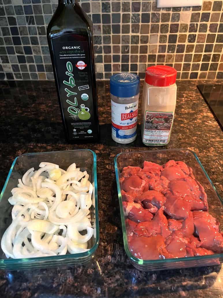 Ingredients for pan-fried chicken liver and onions, including fresh sliced onions, chicken livers, olive oil, salt, and pepper, arranged on a countertop.