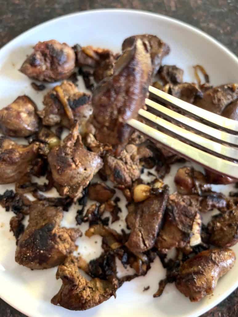 Fork lifting a piece of pan-fried chicken liver from a plate, highlighting the browned exterior and tender texture of the liver.