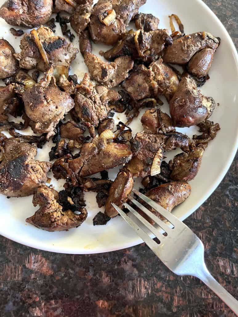 Plate of pan-fried chicken livers with caramelized onions, with a fork resting on the side.