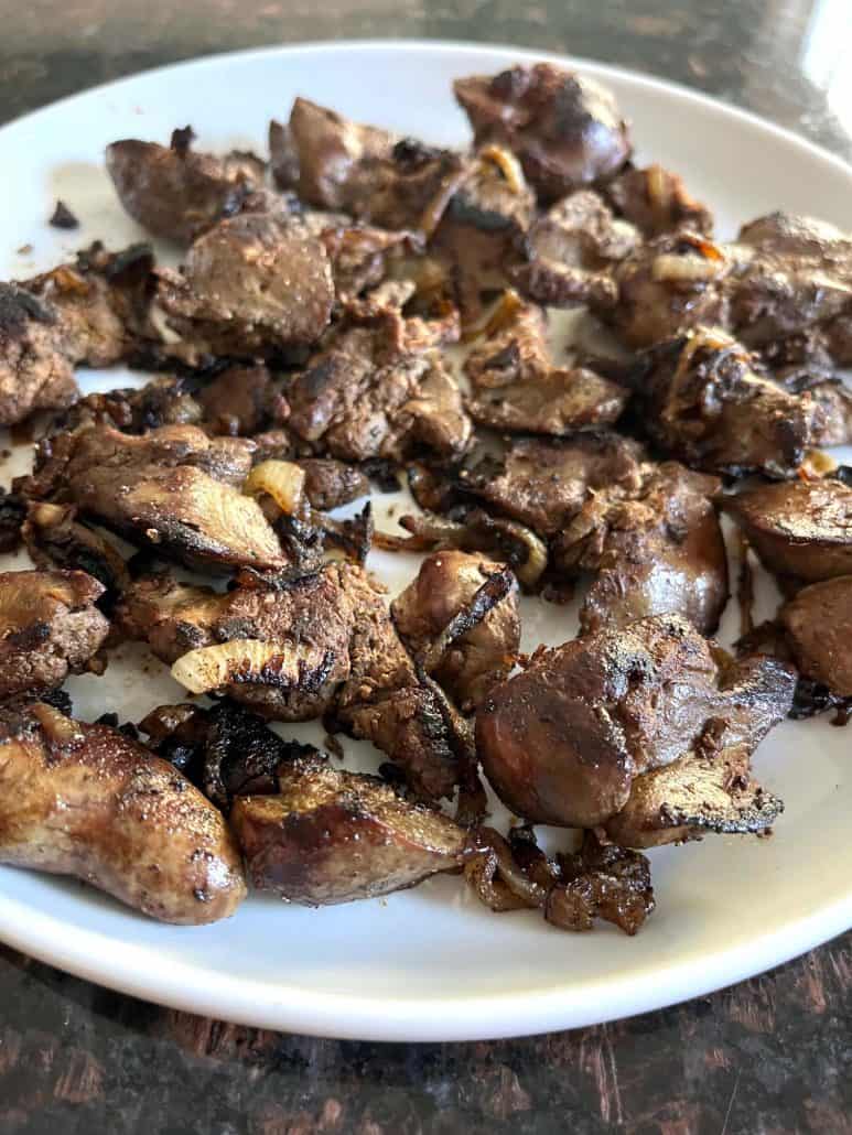 Pan-fried chicken livers and caramelized onions served on a white plate, showcasing the rich, golden-brown texture.