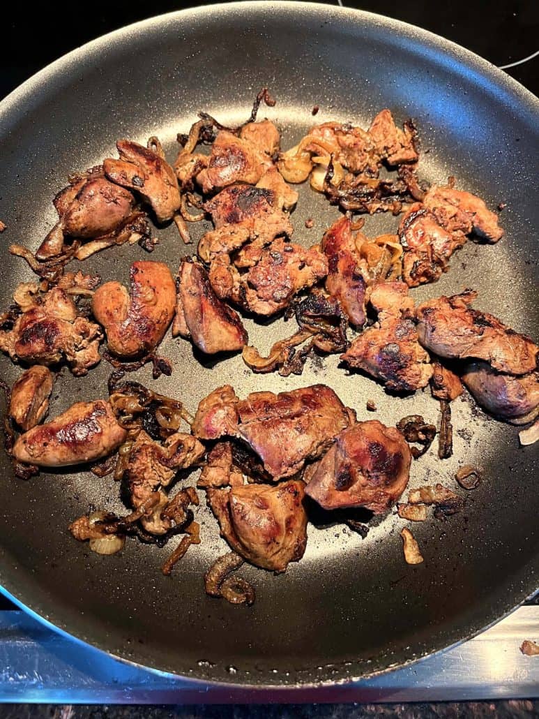 Chicken livers and caramelized onions cooking evenly in a non-stick skillet.