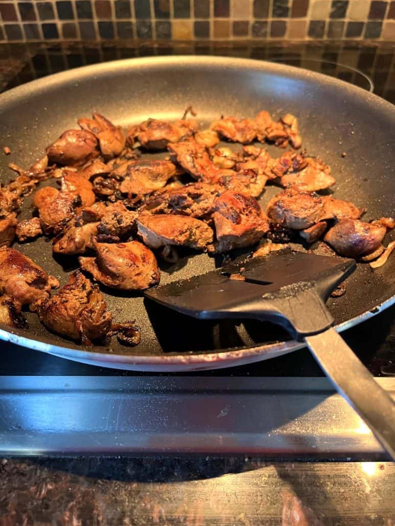 Golden-brown chicken livers cooking in a non-stick skillet, stirred with a spatula.