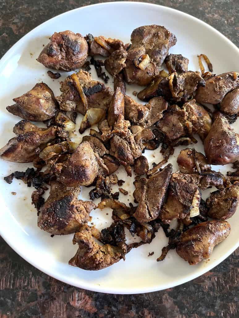 Pan-fried chicken livers with caramelized onions served on a white plate.