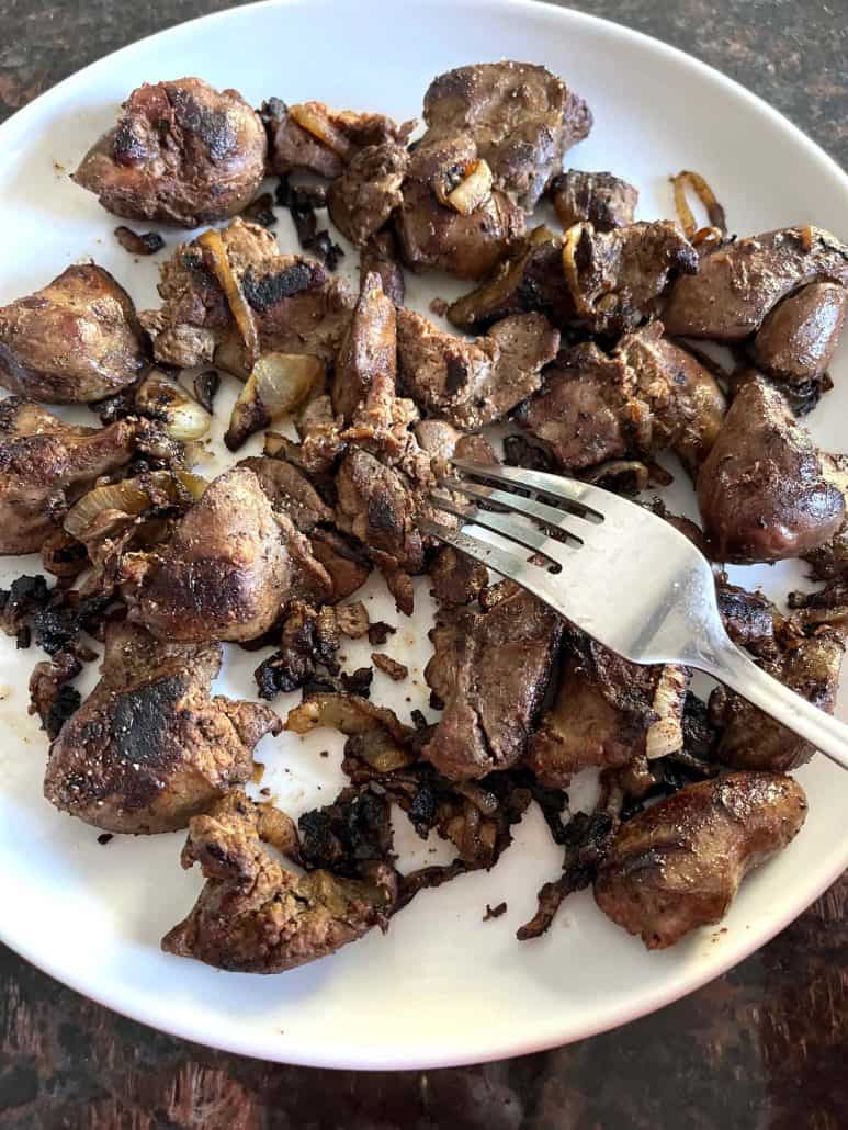 A fork ready to take a bite of chicken livers with caramelized onions.