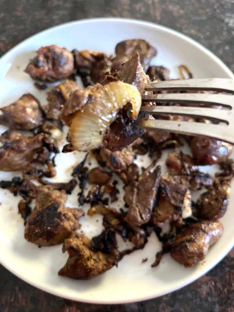 Fork holding a piece of caramelized onion and chicken liver from a plate.