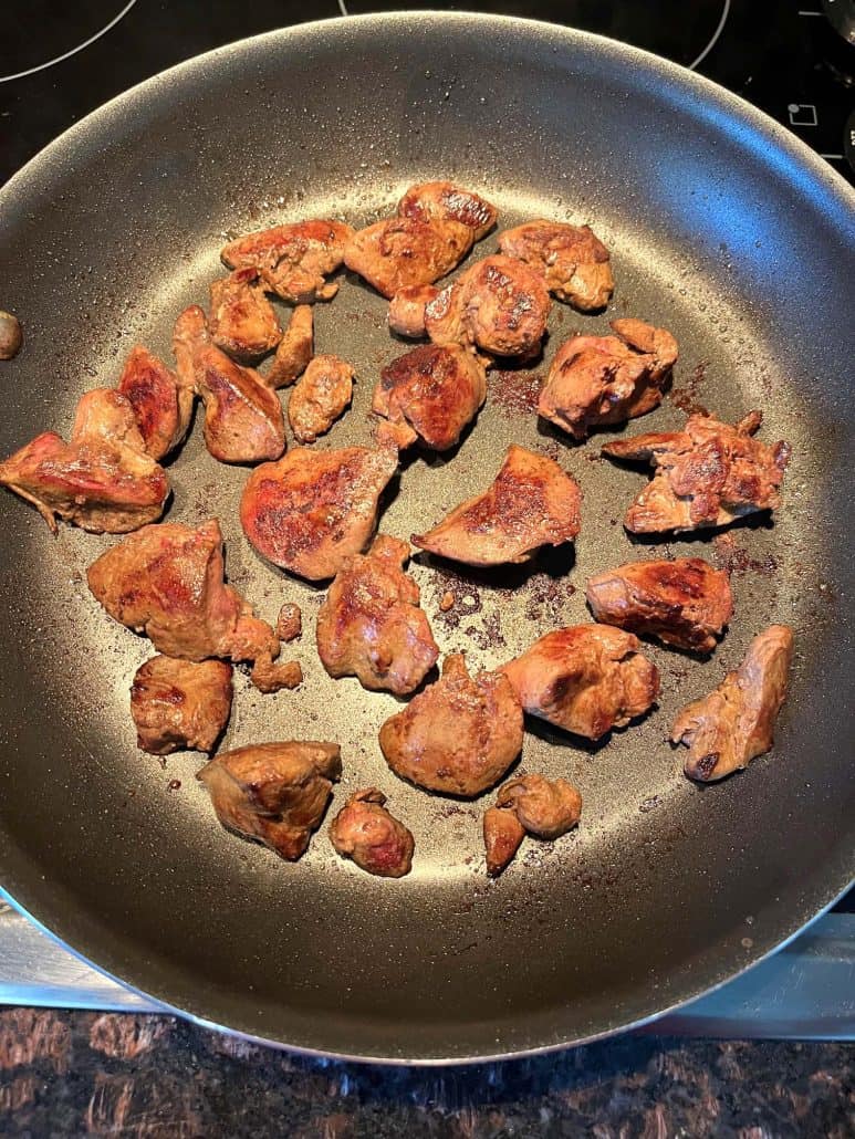 Golden-brown chicken livers cooking in a non-stick frying pan.