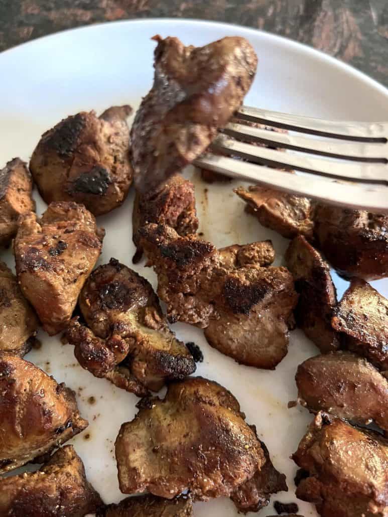 Fork lifting a piece of golden-brown chicken liver from a plate.