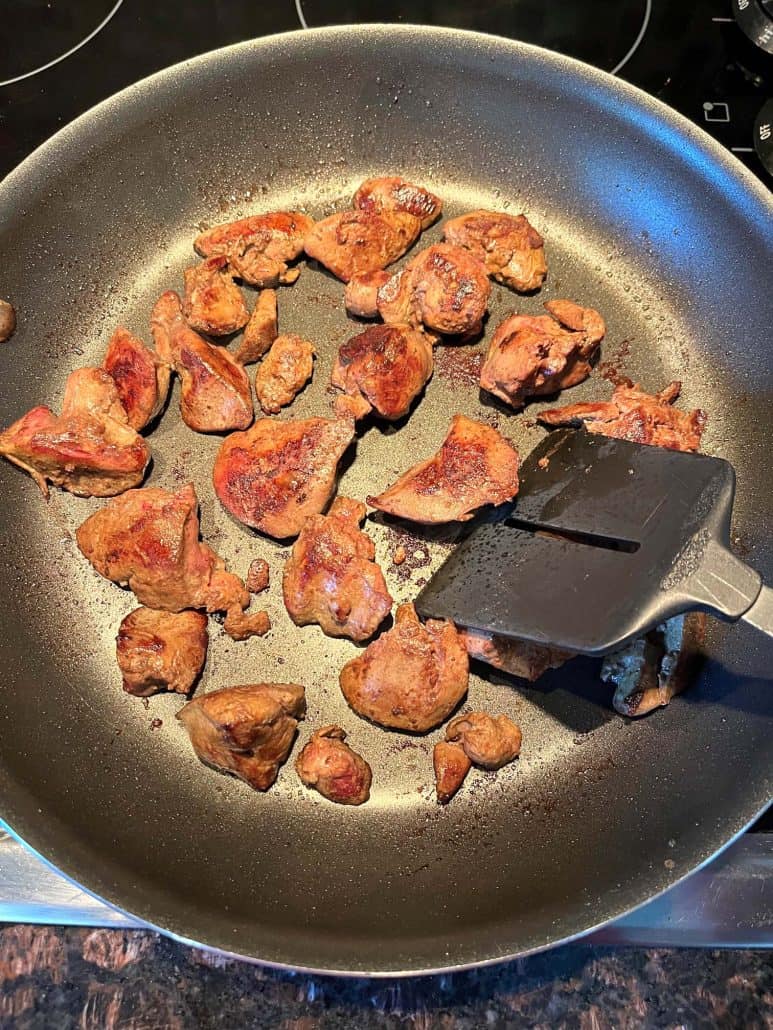 Sauteed chicken livers being cooked in a non-stick pan with a spatula, showing the browning process for a quick and easy recipe.