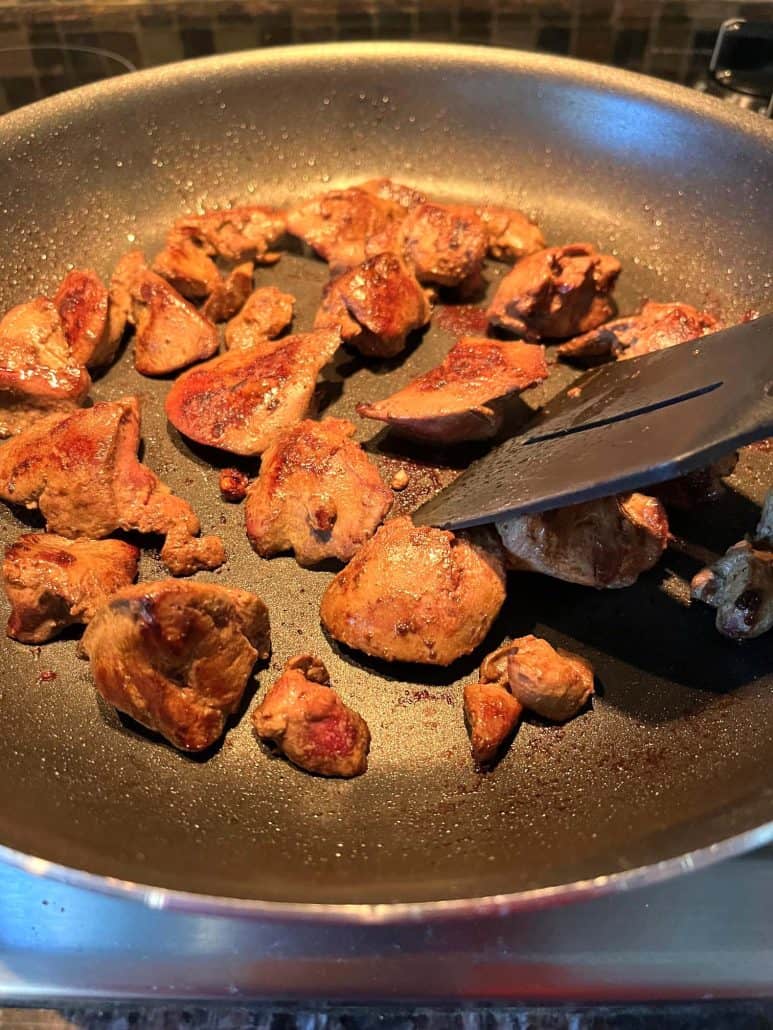 Sauteed chicken livers being stirred with a spatula in a non-stick pan, highlighting the golden-brown finish.