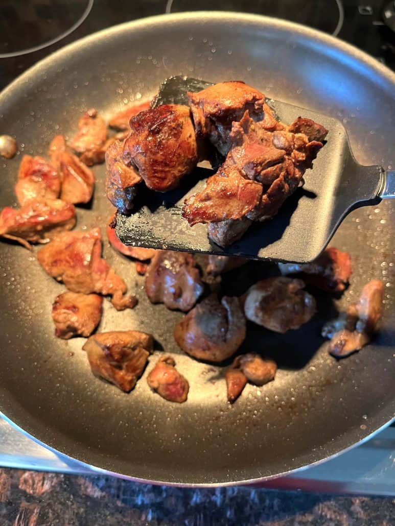 Spatula lifting browned chicken livers in a non-stick pan.