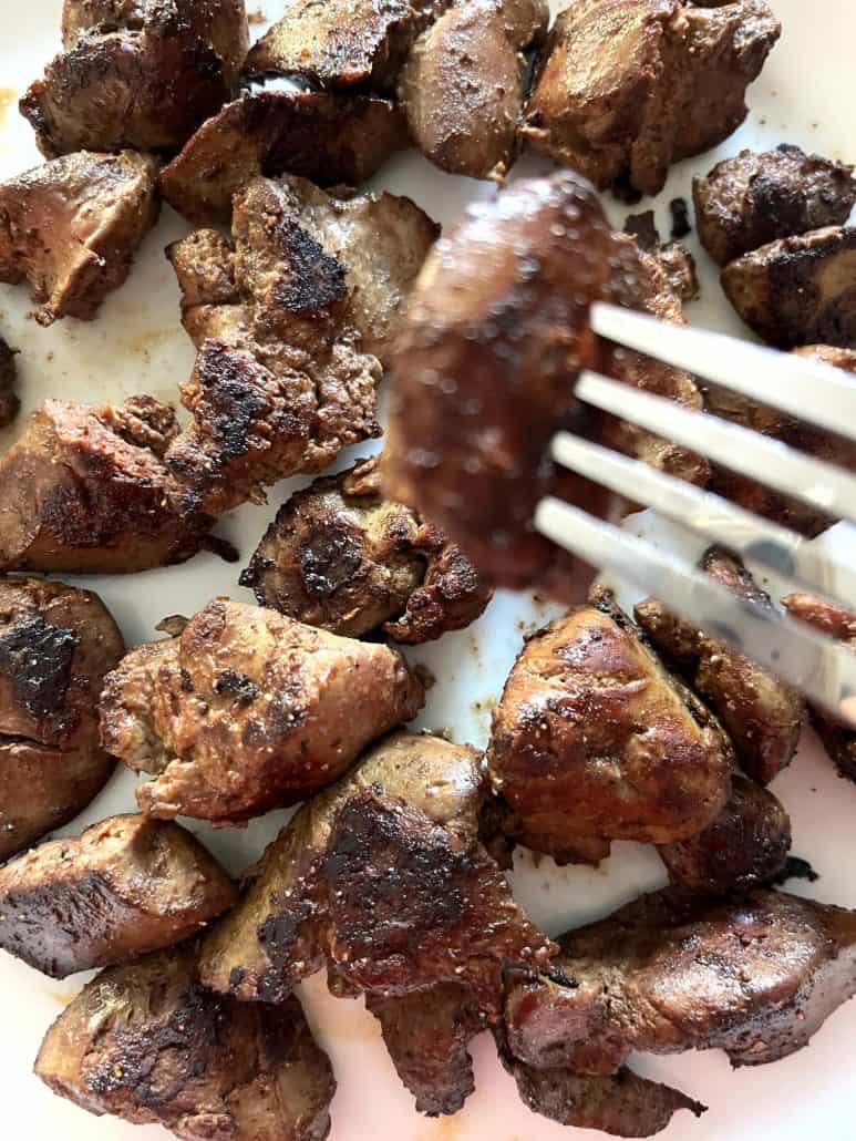 Fork lifting a piece of perfectly browned chicken liver from a plate, highlighting the crispy, seasoned exterior.