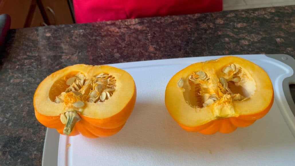 Pumpkin cut in half on a cutting board, showing seeds and pulp inside.