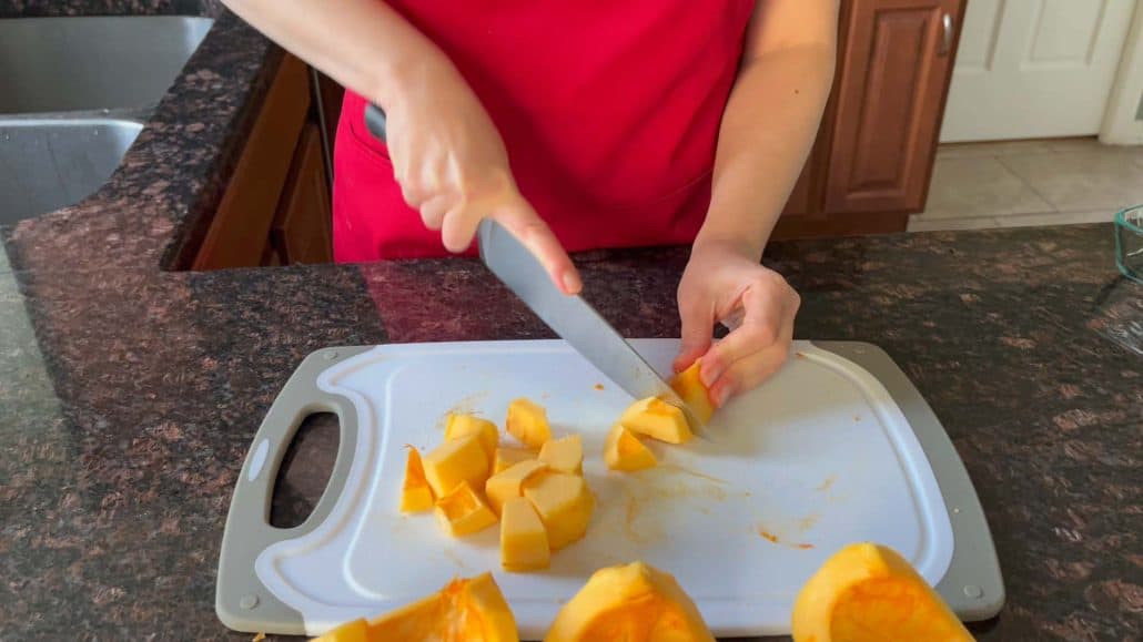 Peeled pumpkin quarters into smaller cubes on a cutting board.