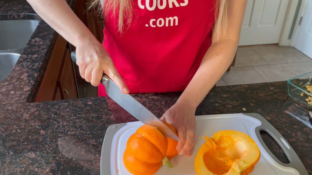 Melanie Mendelson from melaniecooks.com cutting a pumpkin into quarters on a cutting board, preparing it for peeling and cubing.