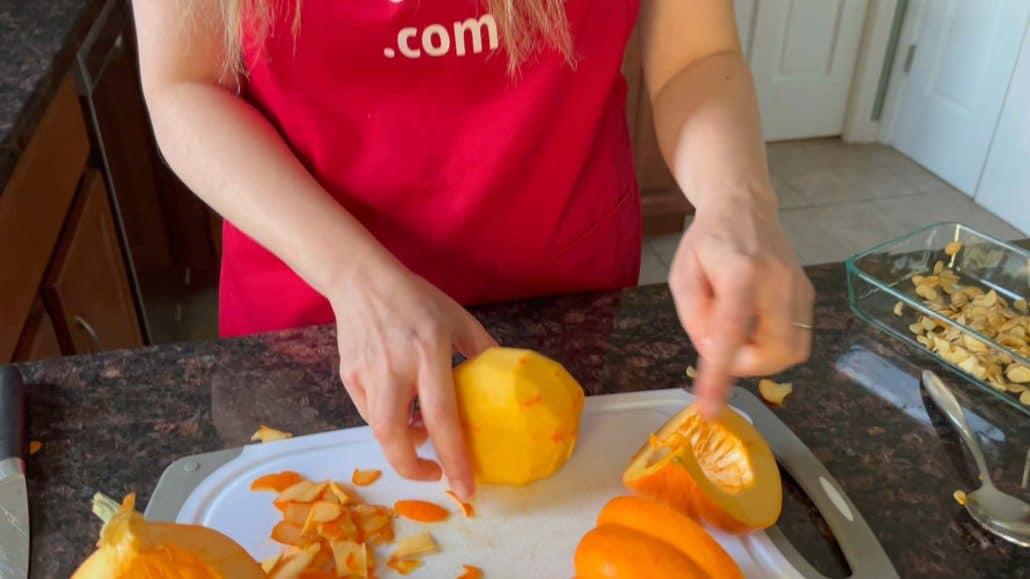 Melanie Mendelson from melaniecooks.com peeling a pumpkin quarter on a cutting board, with prepared pumpkin pieces nearby, ready for cubing.