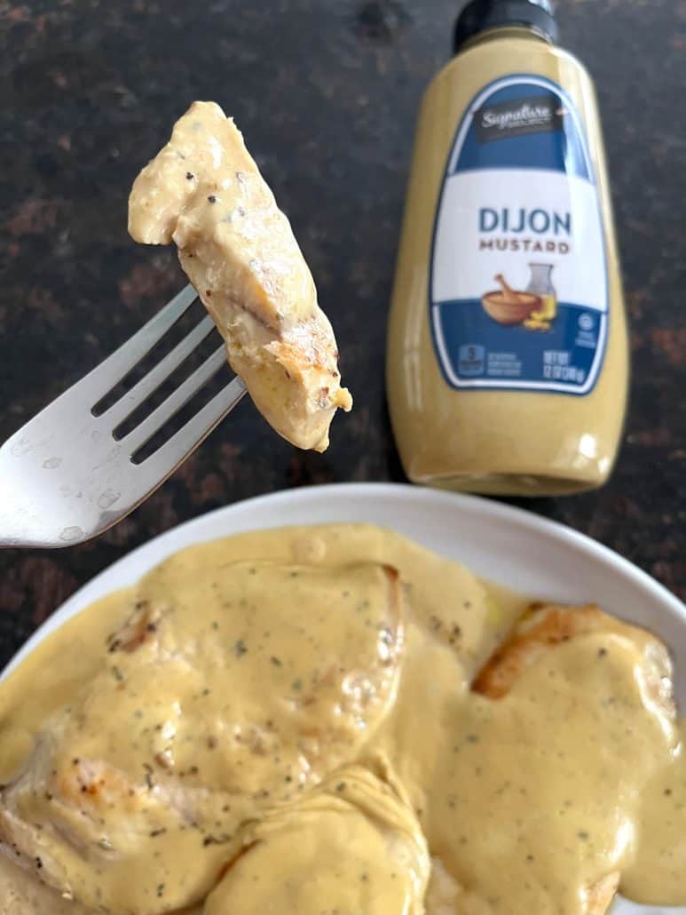 Close-up of a fork holding a bite of juicy Dijon Mustard Chicken, highlighting its creamy sauce.