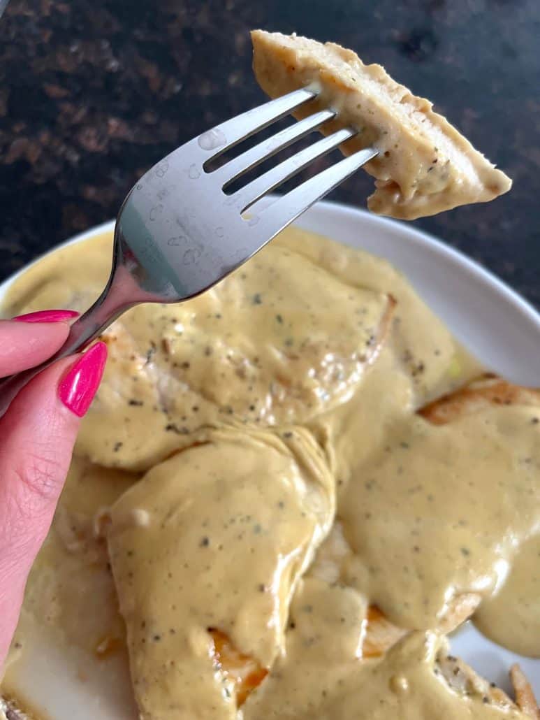 Hand holding a fork with a bite of Dijon Mustard Chicken, highlighting the tender and juicy texture with the creamy sauce in the background.