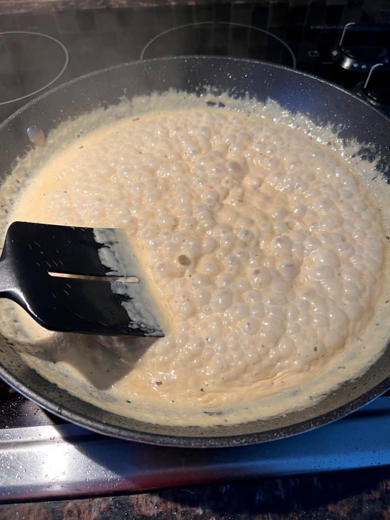 Creamy Dijon mustard sauce bubbling in a pan, being stirred with a spatula.