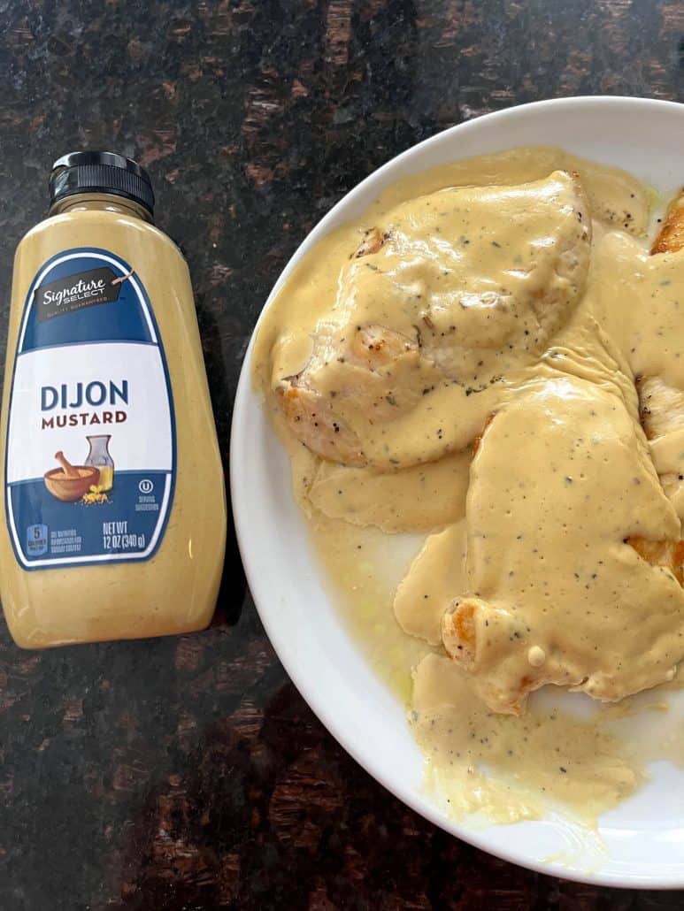 Plate of Dijon Mustard Chicken paired with a bottle of Dijon mustard, highlighting the key ingredient in the creamy and tangy sauce featured in the recipe.